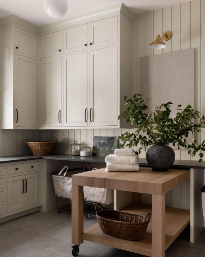 Sage green craft room from @kpdesigns_interiors featuring floor-to-ceiling storage and mobile wooden island.