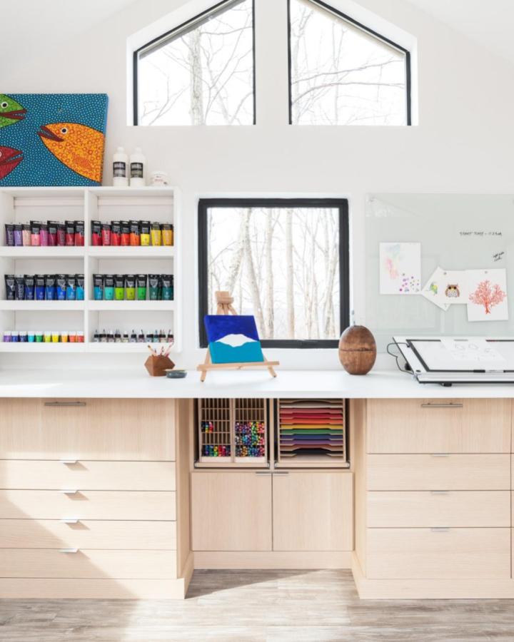 Organized craft room storage with rainbow paint tubes from @calclosets_philadelphia. Light wood cabinets with white countertops and floating shelves.