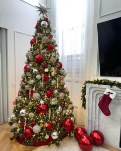 Elegant Christmas tree with metallic starburst topper showcasing red & gold christmas tree ideas from @thetreedresser. Oversized ornaments create dramatic floor display.
