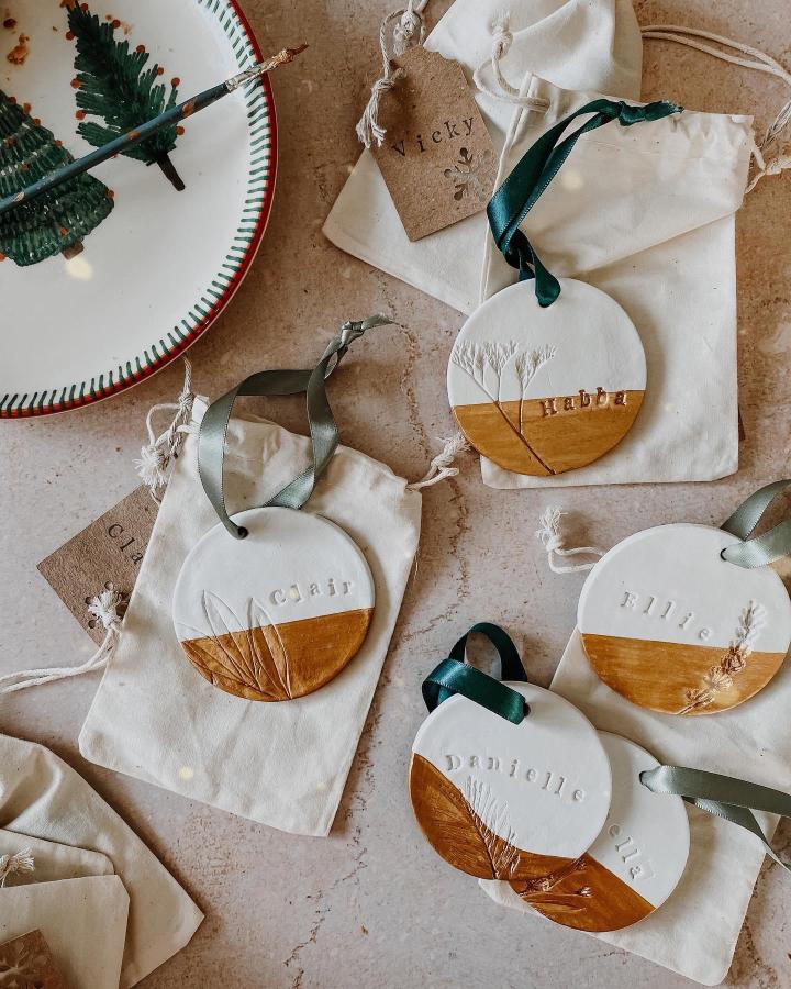 Personalized white and wood ornaments from @laravinckdesigns featuring stamped names and pressed botanicals with silk ribbons.
