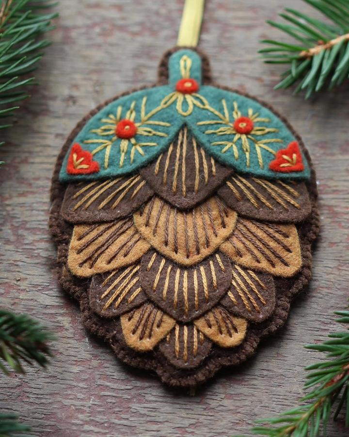 Layered felt pinecone ornament from @kirikipress. Embroidered with golden thread and red bead accents on teal top.