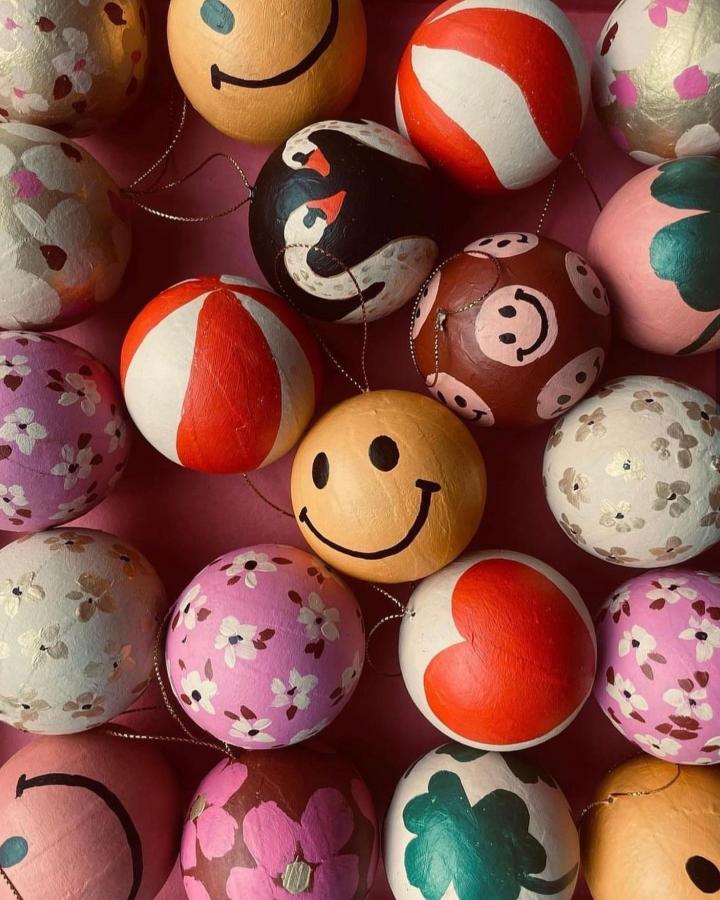 Colorful painted papier mache baubles from @joellewehkamp featuring smiley faces, florals, and penguin designs