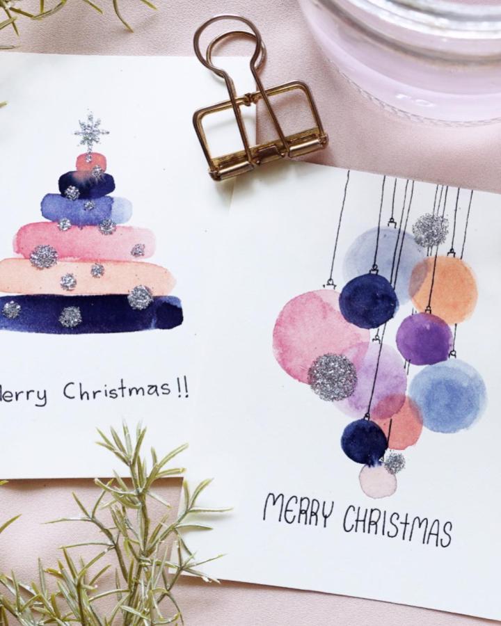 Watercolor christmas card designs from @ig_nianiani featuring painted tree and ornament motifs with glitter details.