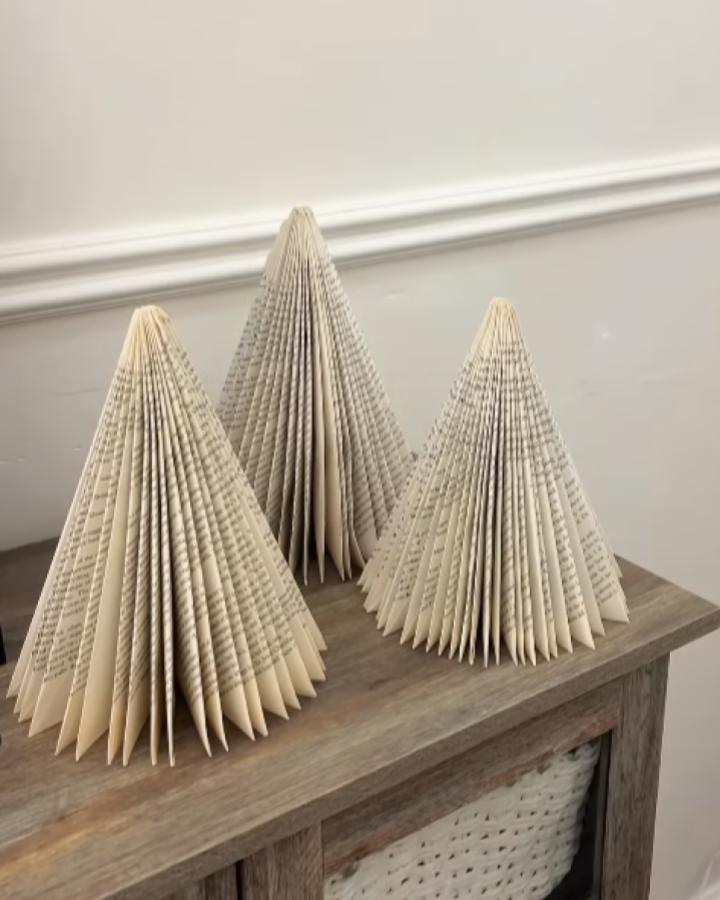 Folded book page christmas crafts for adults from @highburyreno. Three cone-shaped trees on wood surface.