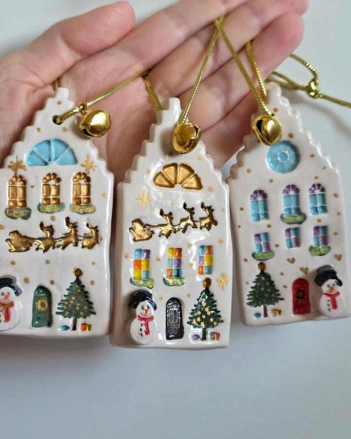 White ceramic house ornaments from @nox_atolye featuring painted windows, golden bells, and festive holiday details.