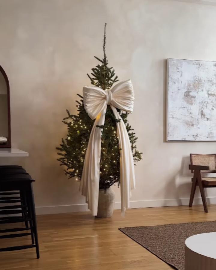 Cream pleated ribbon tree topper from @longbridgelondon. Elegant bow with long trailing tails on decorated tree.