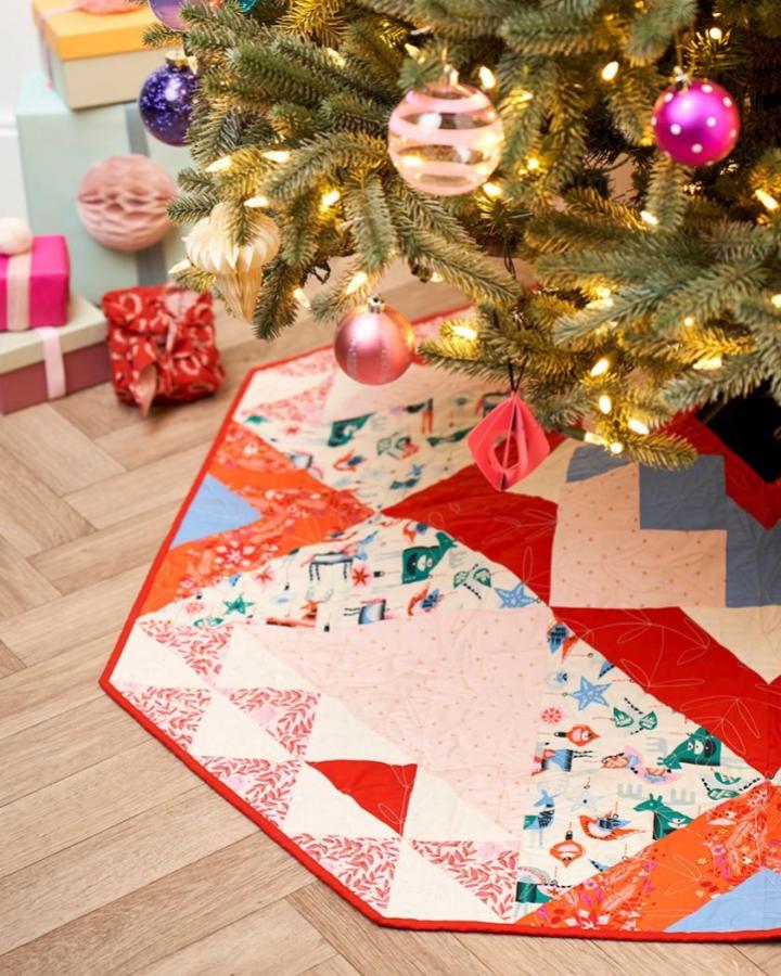 Hexagon patchwork tree skirt from @lovequiltingmag with festive prints and red binding