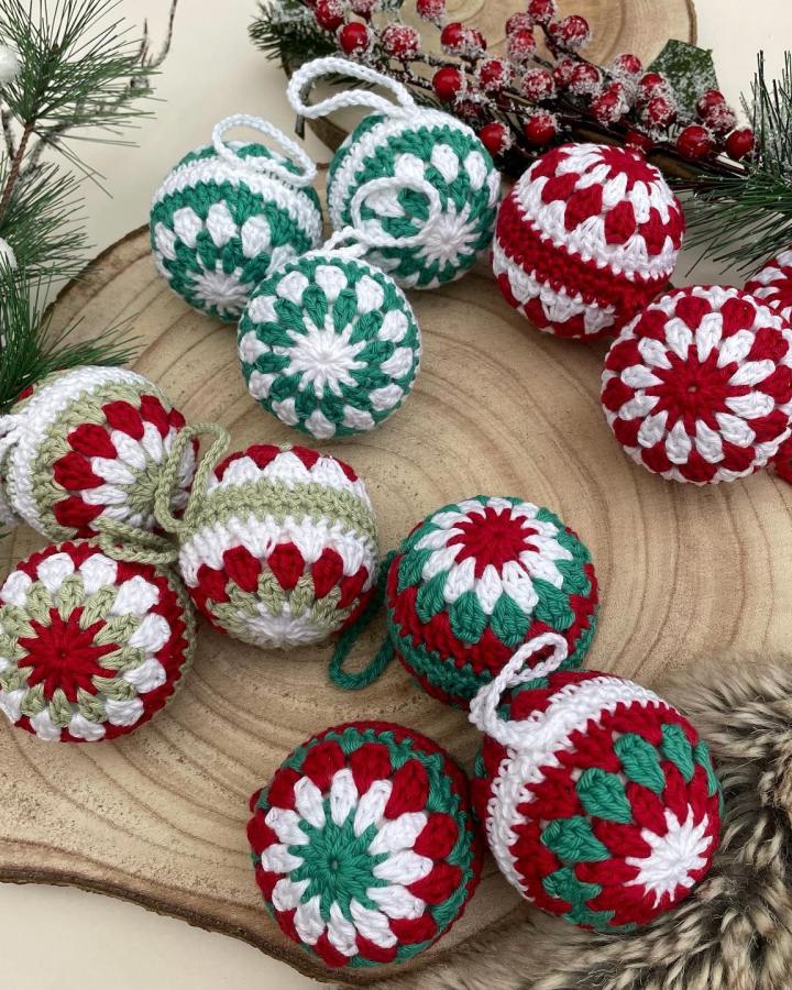 Red, green, and white granny square ornament baubles from @bean_crochet displayed on wood slice with pine.