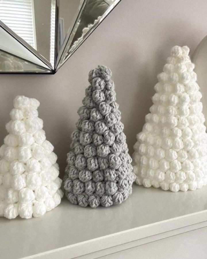 Textured bobble stitch cone trees from @seeloveshare in white and gray yarn on mantel display.