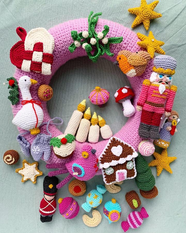 Pink wreath with miniature crocheted holiday characters from @frau_apfelkern featuring nutcracker and candy canes
