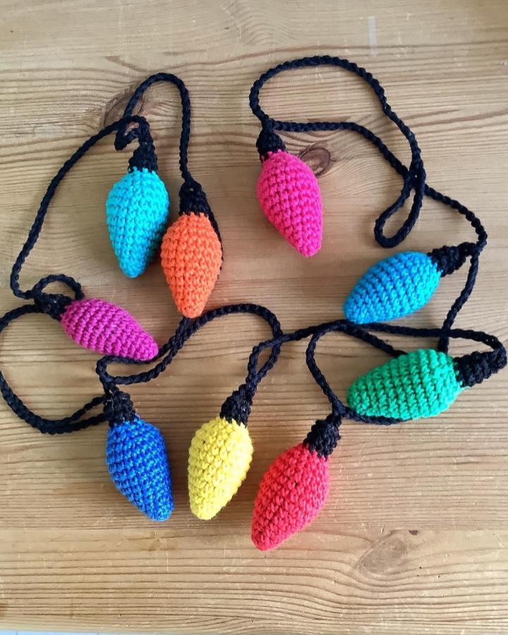 Colorful crochet light bulb garland from @nosewcrow with rainbow shades on black cord