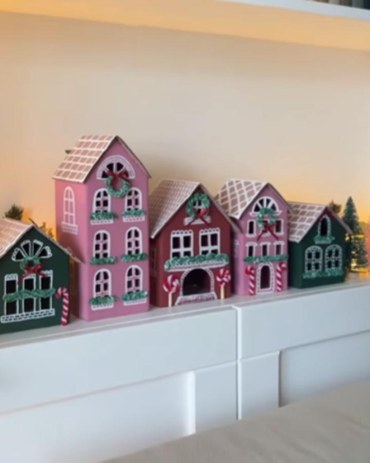 Painted wooden village houses from @bangonstyle featuring pink and green gingerbread-style holiday decorations on white mantel.