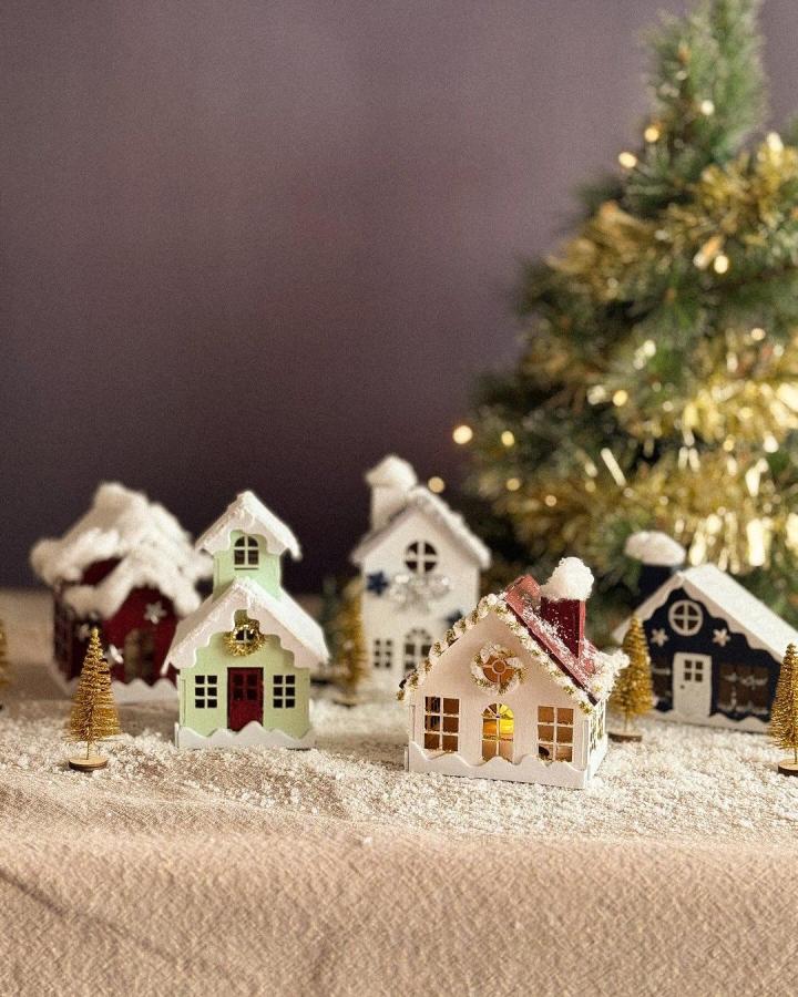 Handcrafted paper village houses from @littlecreationsdiy with snow-dusted roofs and miniature trees surrounding them