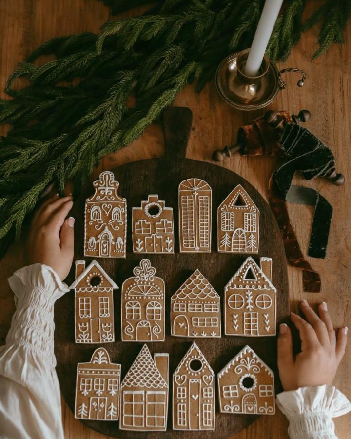 Decorated gingerbread cookie houses from @roxanall_. Arranged on dark wooden board with white icing details.