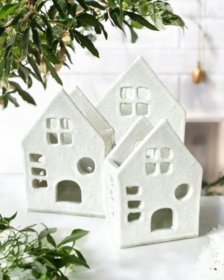 White clay house ornaments from @littlelaneworkshops with cut-out windows arranged in layered composition with greenery.