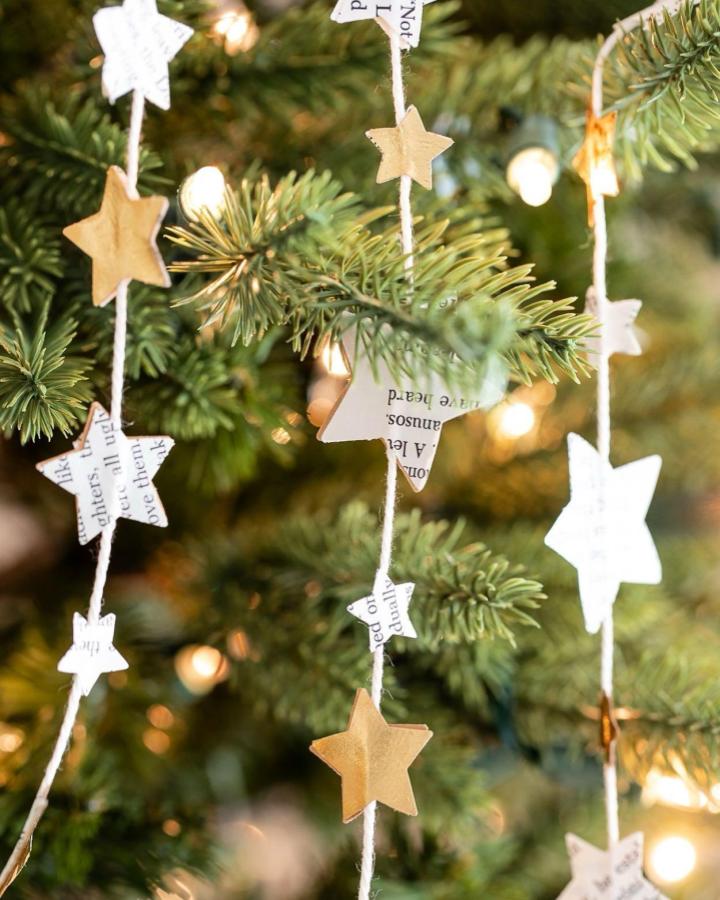 Newsprint and kraft paper star garland from @inspiredbycharm showcasing diy paper garland ideas on evergreen branches with twinkle lights