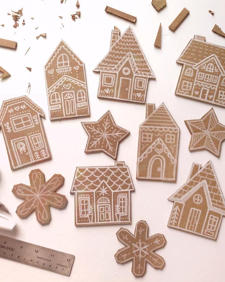 Kraft cardboard gingerbread houses and snowflakes from @tessbelke with white pen decorative details scattered across surface.