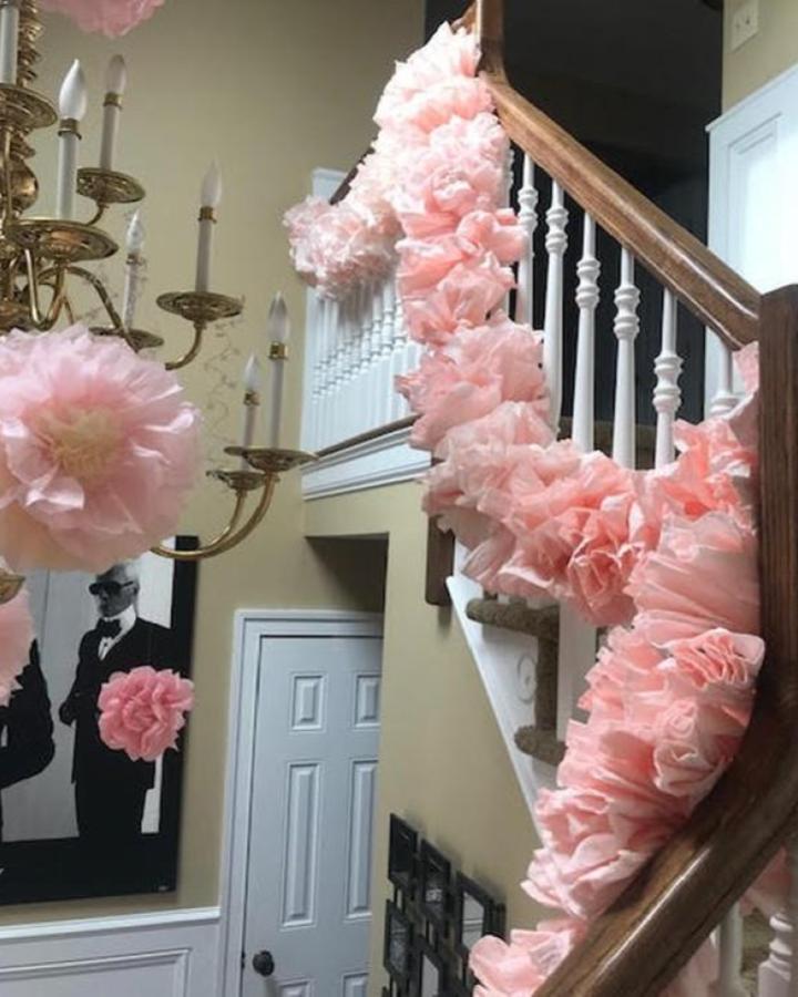 Soft pink tissue paper pom garland from @slrabena draped along wooden staircase banister with vintage chandelier