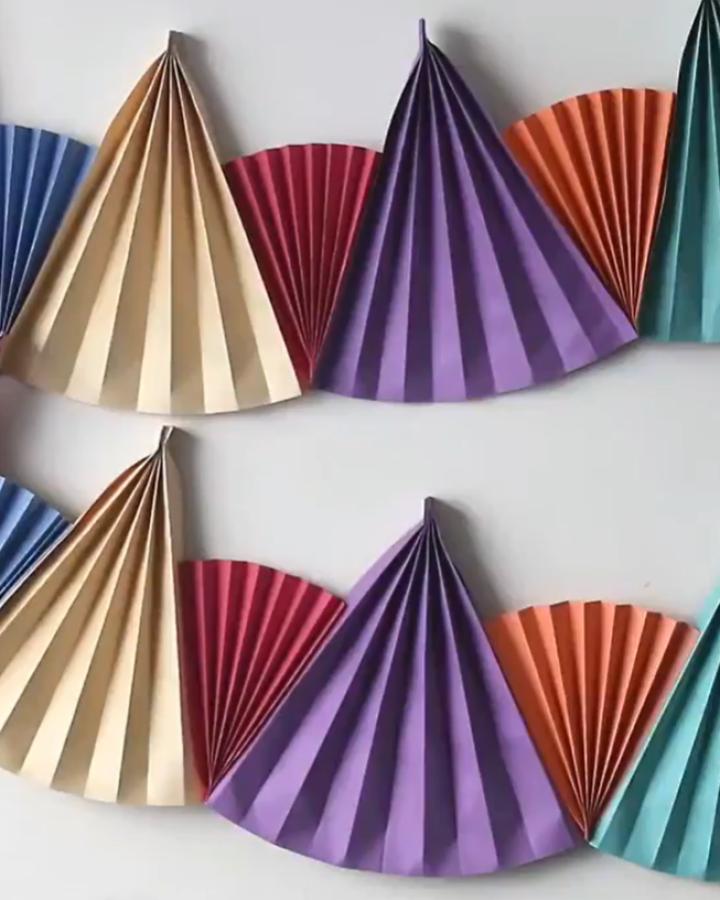Striped accordion paper fans from @ventunoart in purple, coral, cream, and teal arranged as wall decor.