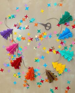 Colorful accordion-folded paper fan garland from @floralflairstudio with scattered star embellishments and vintage scissors.