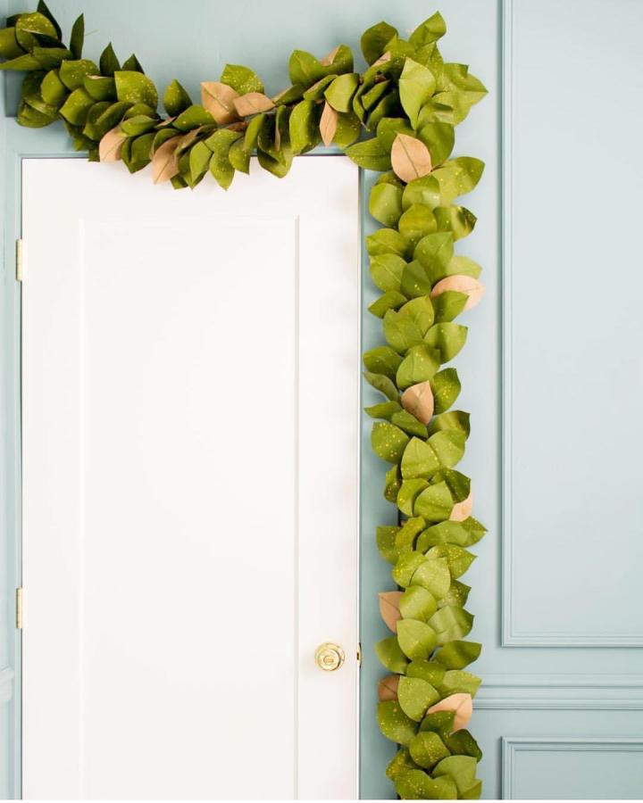 Olive and peach felt magnolia garland from The House That Lars Built draped around white doorframe on blue wall