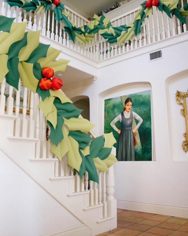 Oversized green and chartreuse paper holly garland from The House That Lars Built with orange berries along white staircase