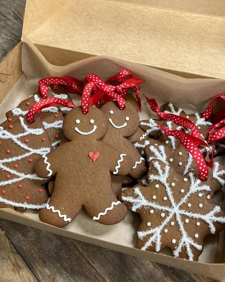 Boxed gingerbread ornaments with red ribbons from @prairiebakingco. White icing details and cheerful faces.