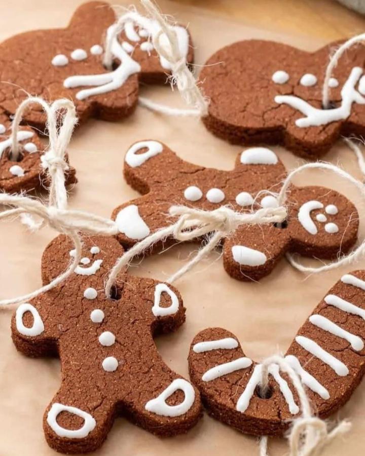 Brown felt gingerbread ornaments from @hellowonderful_co with white icing details and twine hangers on neutral surface