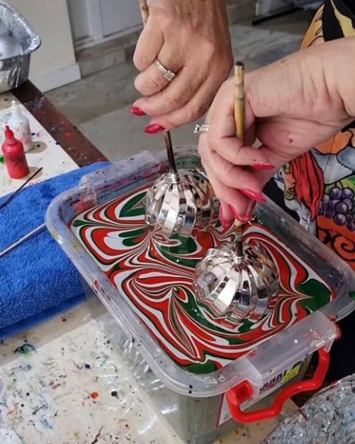 Swirled red and green water marble ornaments for girls night christmas crafts from @raynbowcrowstudios. Hands dipping silver baubles into marbled water.