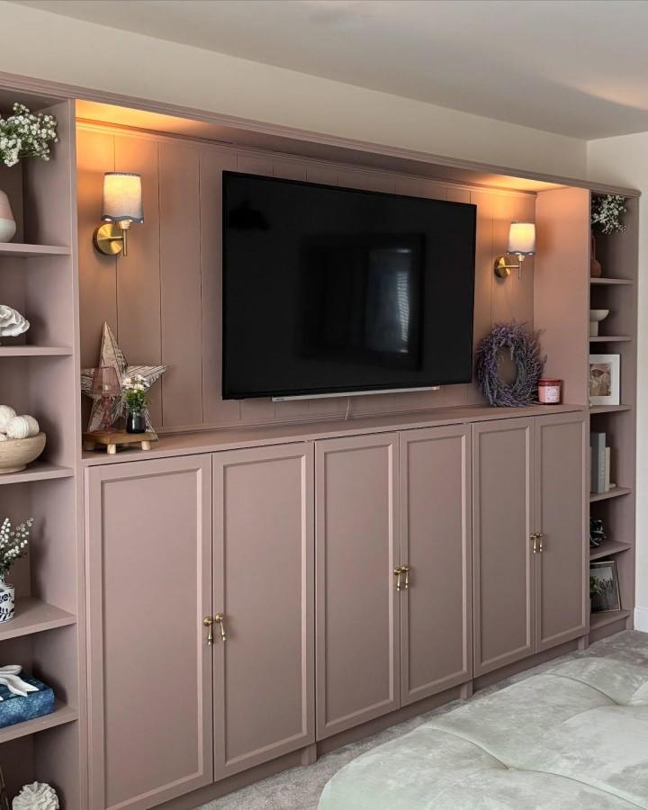 Dusty mauve Billy media wall from @lifewithbecx with brass sconces and styled shelving flanking mounted TV.
