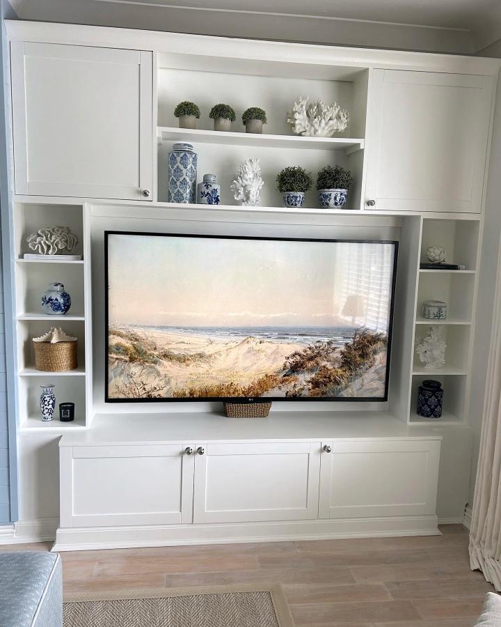 White built-in media wall from @dreah.home with coastal blue ceramics and coral decorative accents displayed.