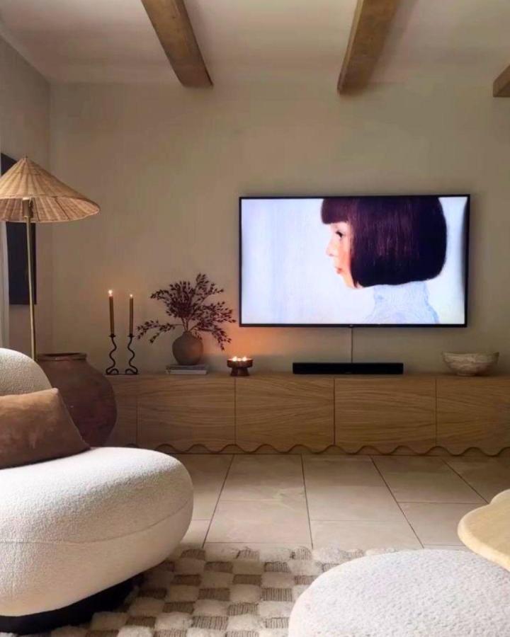Oak-toned media console from @mishkashoe with candlelight, dried botanicals, and mounted screen display.