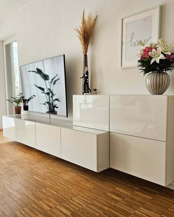 Glossy white floating media console from @diy_home_living with botanical art and warm wood floors.