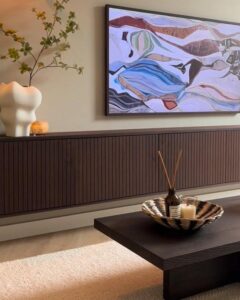 Warm brown ribbed media console from @huisjeinhetpark. Abstract art and sculptural vase create gallery aesthetic.