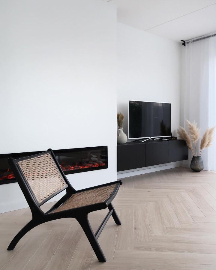 Sleek black floating media console from @byhilalorhan. Minimalist living room with electric fireplace and wall-mounted storage.