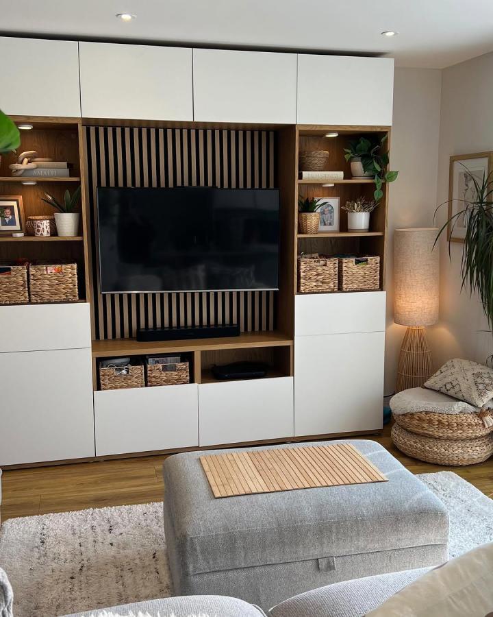 White and wood Besta media unit from @housetohomeuk with vertical slat TV backdrop and woven baskets.