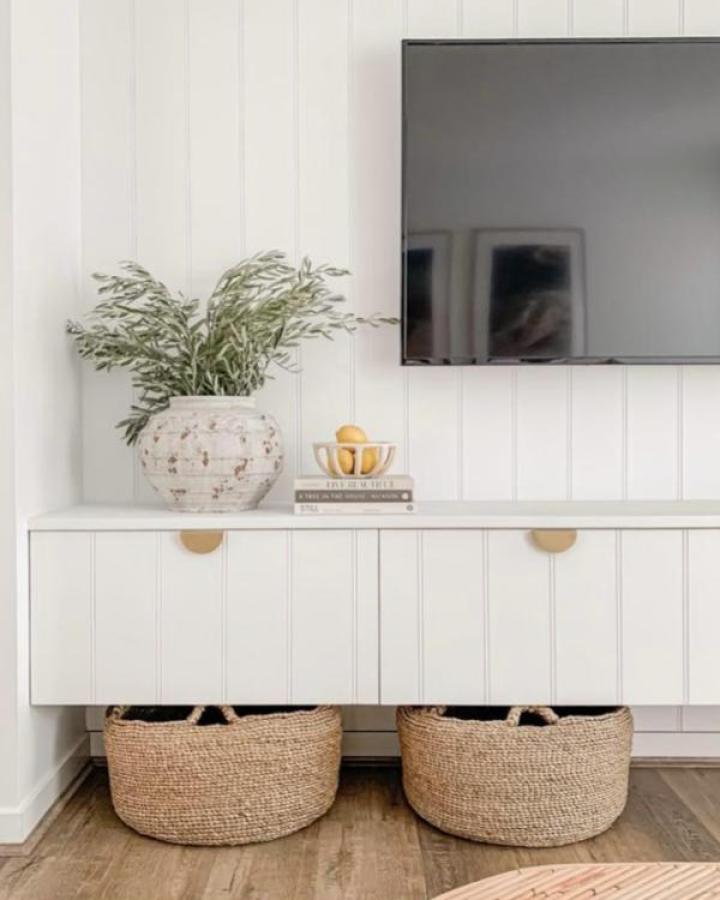 White paneled media console from The Interiors Addict with brass pulls and woven basket storage below.