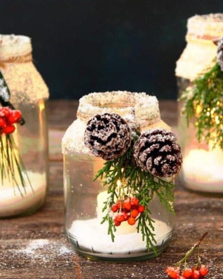 Snowy white mason jar christmas crafts from @roseandrustco featuring frosted pinecones, evergreen sprigs, and red berries.
