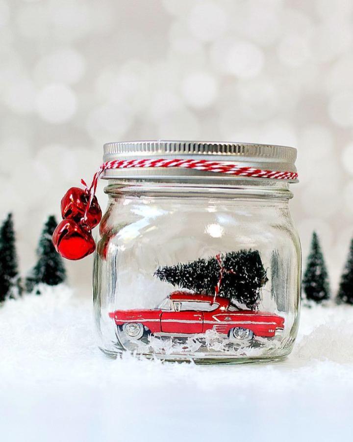 Clear glass jar from @masonjarcraftslove with red vintage car and miniature tree inside snowy scene