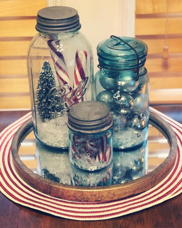 Vintage mason jar christmas crafts from @toriekoski. Three jars filled with ornaments and miniature trees on striped placemat.