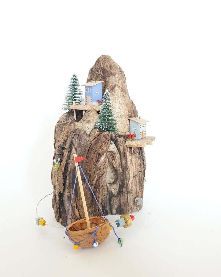 Driftwood village sculpture from @ddimowa with miniature houses and walnut boat below
