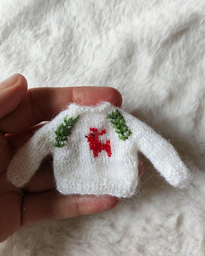 White fuzzy knit sweater ornament from @dailydoll.official featuring miniature christmas crafts & decor with embroidered reindeer and garland details.