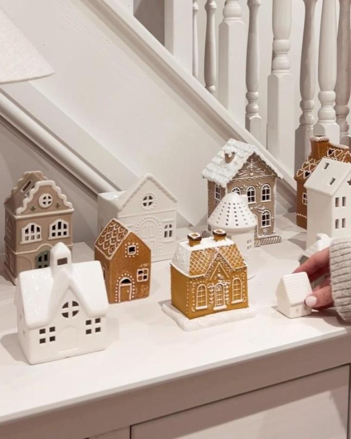Ceramic village houses from @littlehomecomforts displayed on white staircase landing with gingerbread and ivory tones.