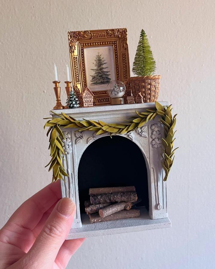 White fireplace mantel from @letties.dollhouse with golden garland and festive holiday accents.