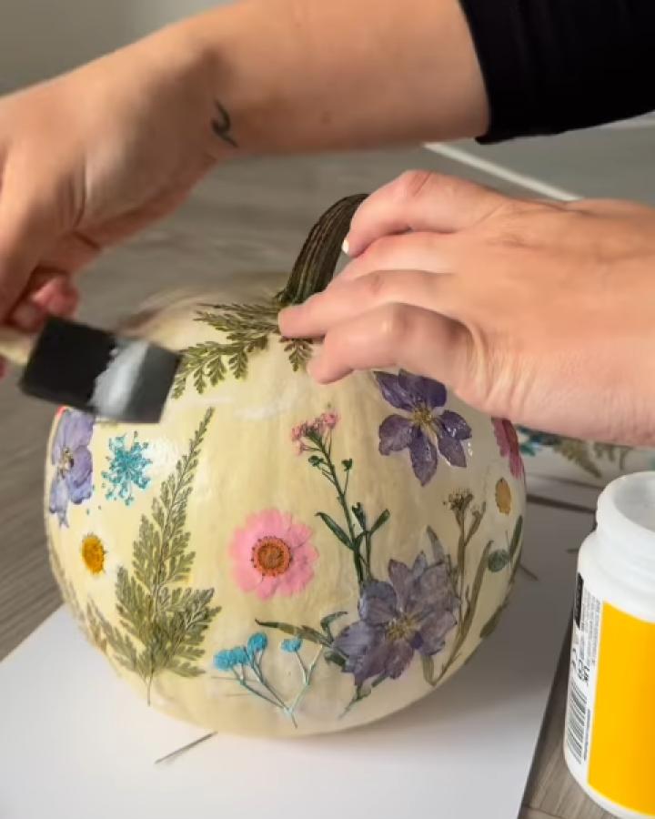 Pressed flower pumpkin crafts for thanksgiving from @myhomeinwiltshire. White pumpkin decorated with colorful dried botanicals and ferns.