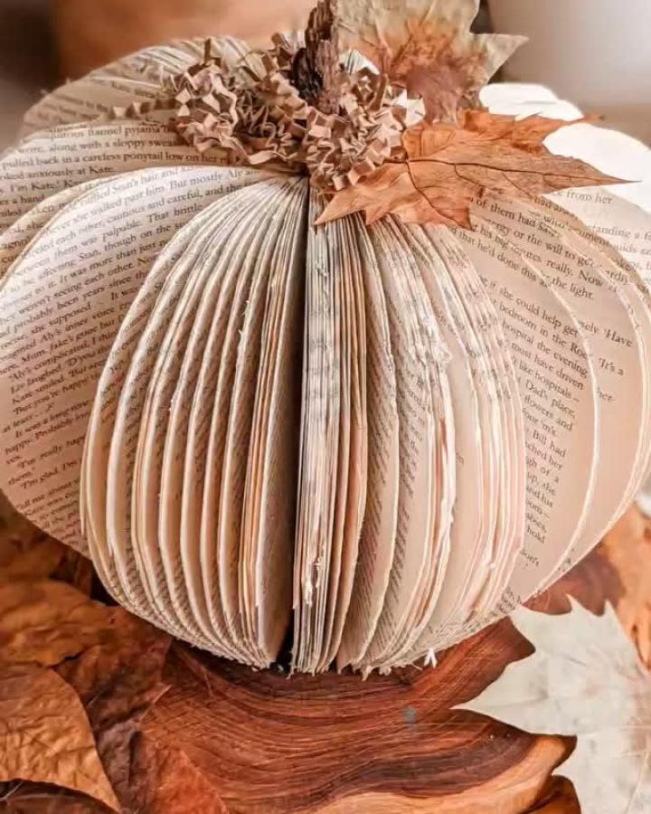 Folded book page pumpkin from @a.playful.day with kraft paper and leaf topper on wood surface