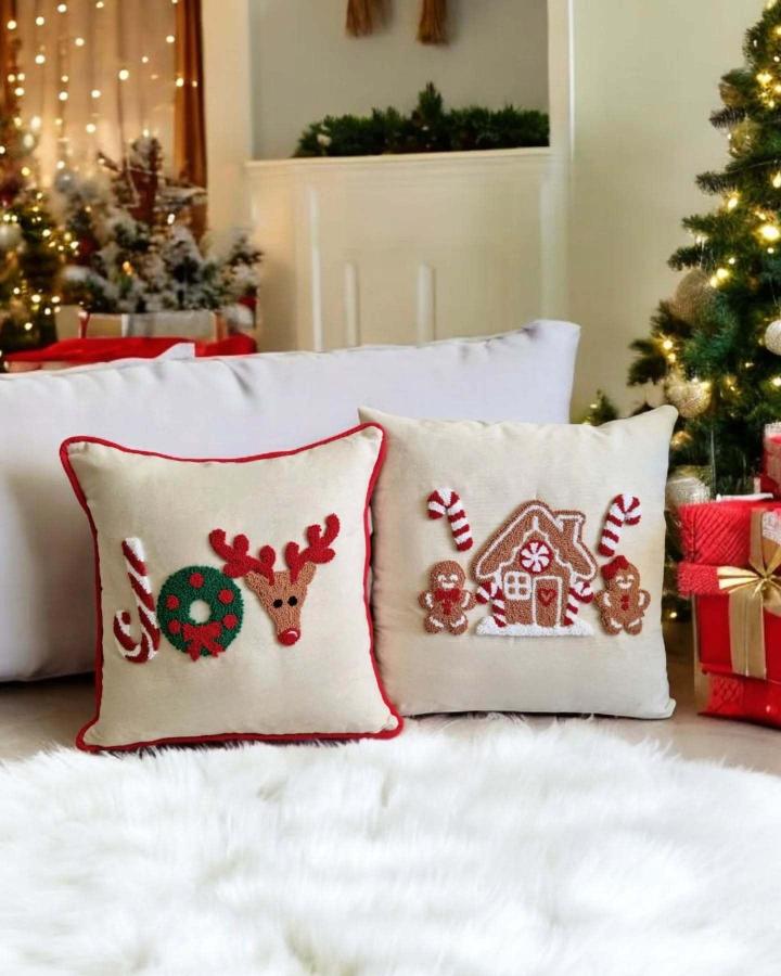 Cream festive pillows from @punchbyguu featuring textured reindeer and gingerbread house designs with red piping
