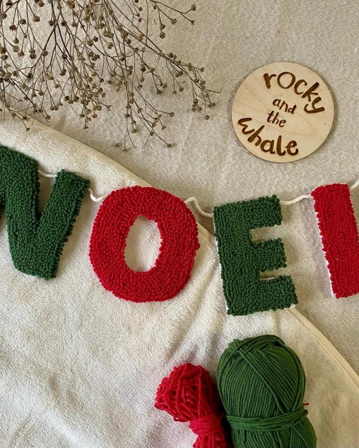 Textured punch needle christmas decorations from @rockyandthewhale spelling NOEL with red and green yarn on cream fabric