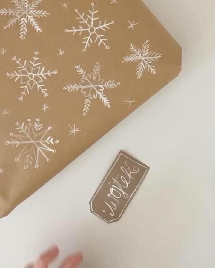 White snowflake drawings on kraft paper wrapping from @thefoxintheattic with hand-lettered gift tag detail.