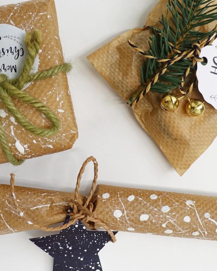 Speckled brown kraft paper gifts from @ilovebacofoil with twine, greenery, and gold bells.